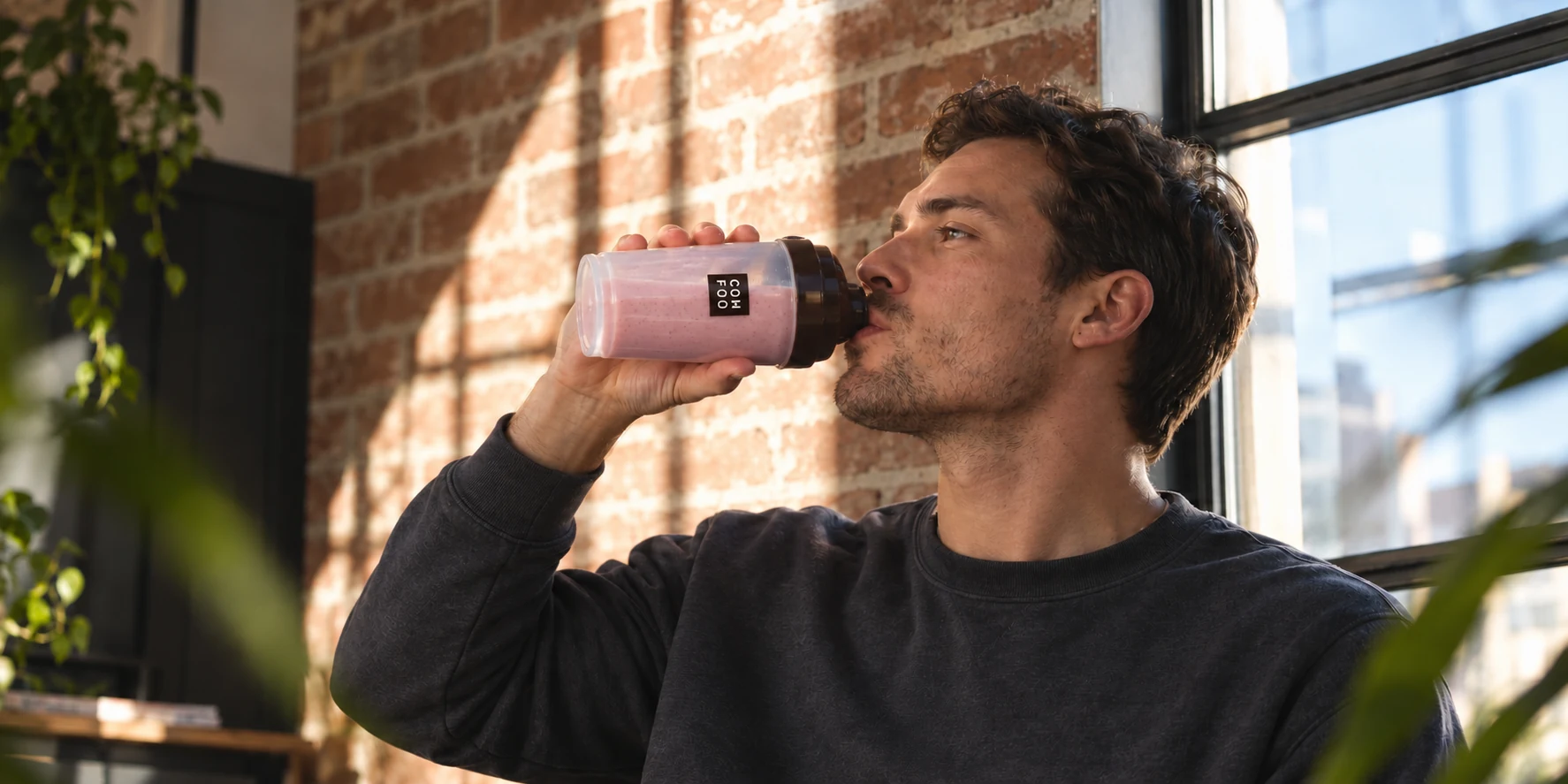En man dricker en rosa ComFoo-shake vid ett fönster